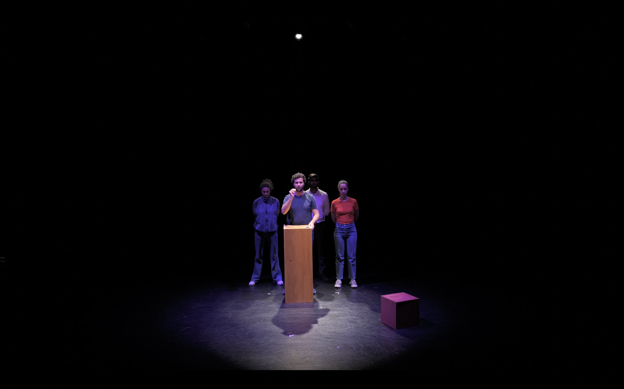Quatre personnages rassemblés sur le plateau autour d’un pupitre.