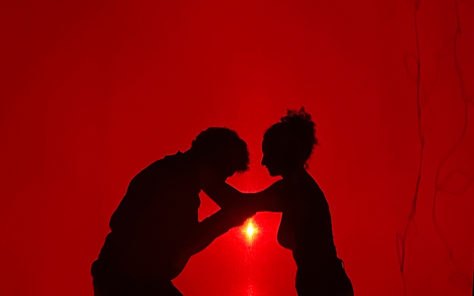 Deux silhouettes se font face en théâtre d’ombres sur un fond rouge.